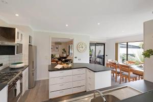 a kitchen with white cabinets and a dining room at Kookaburra Beach House - 3 bedroom home in Tura Beach +25 photos