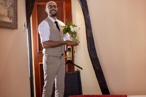 Un hombre parado frente a una puerta sosteniendo un jarrón de flores. en Hôtel Des Marronniers, en París