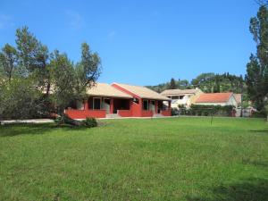 a red house with a green lawn in front of it at LEFKES Apartments Sidari in Sidari