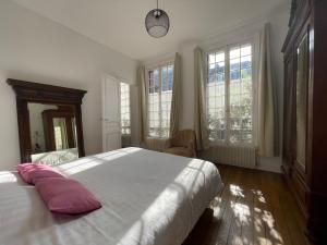 una camera da letto con un grande letto bianco con cuscini rosa di Chez Hélène, calme et verdure au centre historique a Vincennes