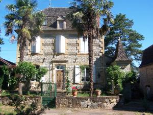 una vieja casa de piedra con palmeras delante en Domaine de Granval Chambres d'Hôtes, en Bretenoux