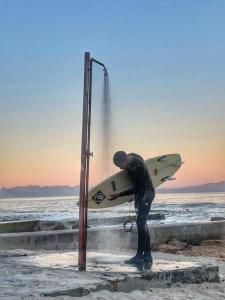 un hombre de pie en la playa sosteniendo una tabla de surf en Cottage, Nine on Windsor, Kalk Bay, Cape Town, en Kalk Bay