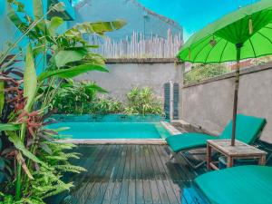 a swimming pool with a green umbrella and a chair and a table at The Green Home Bali in Denpasar
