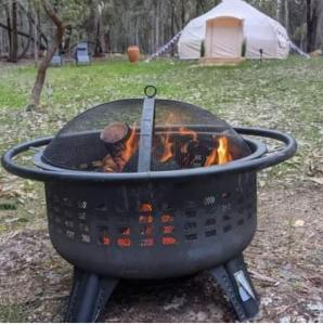 a grill with fire in it with a tent in the background at Eversprings Glamping in Mount Helena