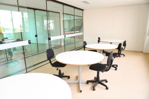two tables and chairs in an office with glass walls at Hotel Plaza Garden in Cascavel