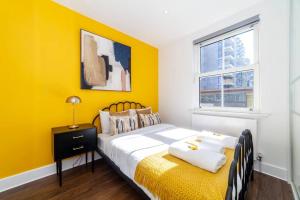 Dormitorio amarillo con cama y ventana en Central 4BDR home wgarden & parking en Londres