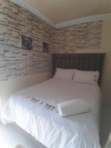 a bedroom with a white bed with a brick wall at LINGE'S LODGE EXTENSION in Lusikisiki