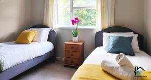 two beds in a bedroom with a vase of flowers on a table at Cambridge Stays 3BR House-Garden-Lots of Parking-15 min to City Center- Close to Cambridge Science park in Cambridge