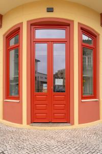 a red door on a building with three windows at A'MAR by Alojamento Ideal in Póvoa de Varzim