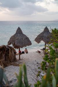 two people sitting under straw umbrellas on a beach at Waterside Apartments in Willemstad