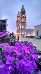 una torre del reloj con flores púrpuras delante de ella en Hotel Maya Ah Kim Pech en Campeche