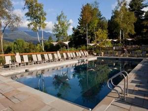 a swimming pool with lounge chairs and trees and mountains at Topnotch Retreat in Stowe