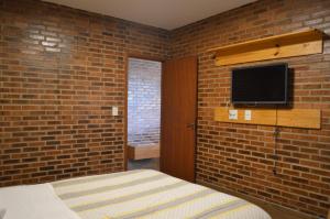 a brick walled bedroom with a bed and a tv at Chalés Estrada Real in Conceição da Ibitipoca