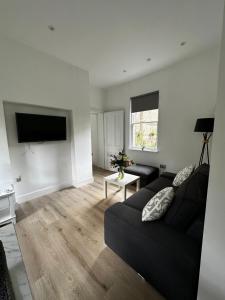 a living room with a black couch and a flat screen tv at Flat 2 The Butlers Quarters in Oswestry