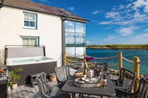 eine Terrasse mit einem Tisch und Stühlen sowie einem Whirlpool in der Unterkunft Hen Cymyran in Caeʼr-geiliog