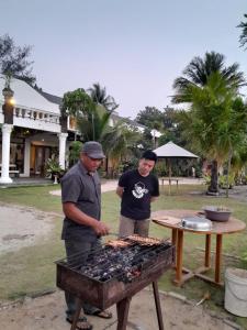 Dois homens estão a cozinhar comida num grelhador. em Keraton Krakatoa em Banten