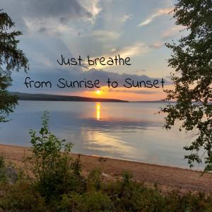 a sunset over the water with the words just breathe from sunrise to sunset at Arctic Circle Beach House in Meltosjärvi