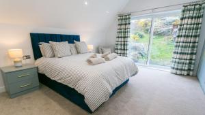 a bedroom with a bed with a blue headboard and a window at Sirusa in Trearddur