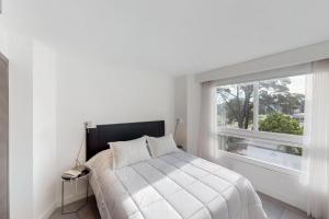 a white bedroom with a bed and a window at Oceana Suites en Yoo, con piscina interior climatizada in Punta del Este