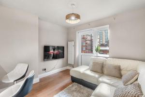 Central Whitechapel - Steps from Station & Sights! في لندن: غرفة معيشة مع أريكة بيضاء وتلفزيون