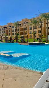 a large blue swimming pool with palm trees and a building at Ultra Luxury 3BR with Pools ,Sports ,Dining in Gated compound, Close to all sites in Cairo