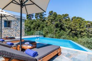 a pool with chairs and an umbrella next to a house at Petrino Villas in Skopelos Town