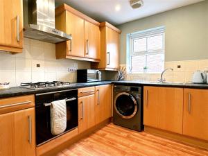 cocina con armarios de madera, lavadora y secadora en Cheerful two-bedroom townhouse near Leeds and York, en Leeds