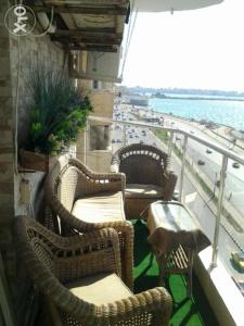 een balkon met rieten stoelen en tafels en uitzicht op de oceaan bij شقه للإيجار المفروش سوبر لوكس (vip) أمام البحر مباشرة in Alexandrië