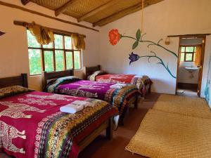 three beds in a room with a painting on the wall at PONDOWASI LODGE in Ibarra