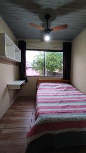 een slaapkamer met een bed, een plafondventilator en een raam bij Casa completa com 2 quartos de casal em Torres in Torres
