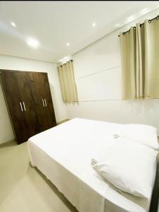 um quarto com uma cama branca e um armário de madeira em Apartamentos Villa dos Diamantes em Porto Seguro
