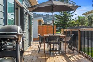a patio with a table with an umbrella and a grill at Recline on Leo in Waihi Beach