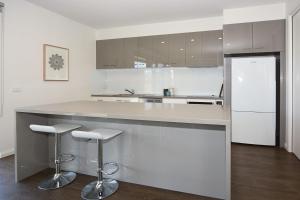 a white kitchen with a counter and stools in it at Rolling Waves in Pt Leo in Shoreham