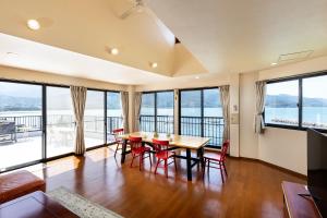 Rakusansui Villa في Itoshima: غرفة طعام مع طاولة وكراسي ونوافذ كبيرة
