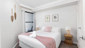 een witte slaapkamer met een wit bed met roze accenten bij On the Beach Getaway in One Mile