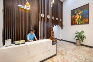 a man standing behind a reception desk in a lobby at RAON Hotel - STAY 24H in Quy Nhon