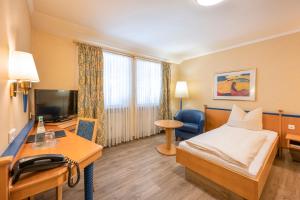 ein Hotelzimmer mit einem Bett, einem Schreibtisch und einem TV in der Unterkunft Hotel Neuwirt in Sauerlach