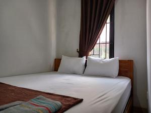 a bed with white sheets and pillows in a room with a window at OYO 93085 Homy Stay Syariah in Balikpapan