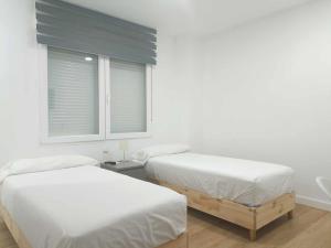 2 camas en una habitación blanca con ventana en Casa de Huéspedes 12 Octubre Rooms, en Madrid