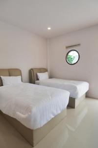 two beds in a white room with a window at Chanmuang Resort ชานเมืองรีสอร์ท in Phetchaburi