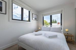 a white bedroom with a large white bed with two windows at Trendy and Spacious Brunswick Stay with Outdoor Deck in Melbourne