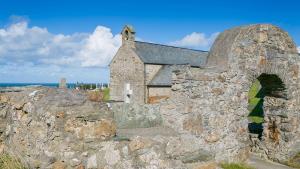 an old stone building with an arch in front of the ocean at Anchor Cottage in Cemaes Bay