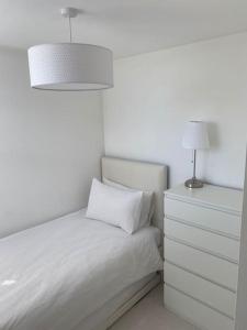 a white bedroom with a bed and a nightstand with a lamp at Large 2 Bed Maisonette, walking distance to Centre in Cardiff