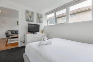 a white bedroom with a bed and a tv at Bright and Modern Space with a Balcony and Parking in Melbourne