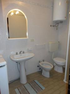 een badkamer met een wastafel, een toilet en een spiegel bij Wonderful apartment with terrace and pool in Porto Santa Margherita di Caorle