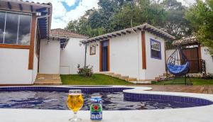 a glass of beer sitting on a table next to a house at Flat com Piscina no Centro de Tiradentes in Tiradentes