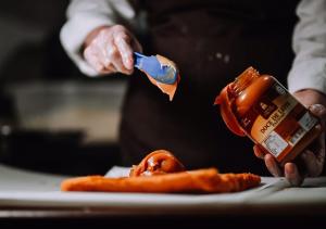 a person holding a bottle of sauce and a plate of food at Hotel Chalé Capitólio in Capitólio