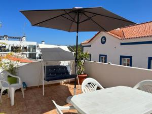a patio with an umbrella and a table and chairs at Casa com Cor in Zambujeira do Mar