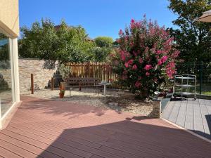 a wooden deck with a bench and a bush with pink flowers at Le Relais de Choz in Chozeau