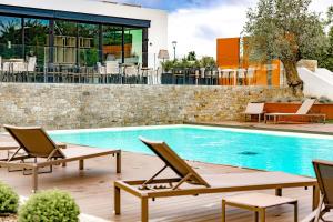 - une piscine avec 2 chaises longues à côté d'un bâtiment dans l'établissement Hôtel Parc du Landreau, aux Herbiers